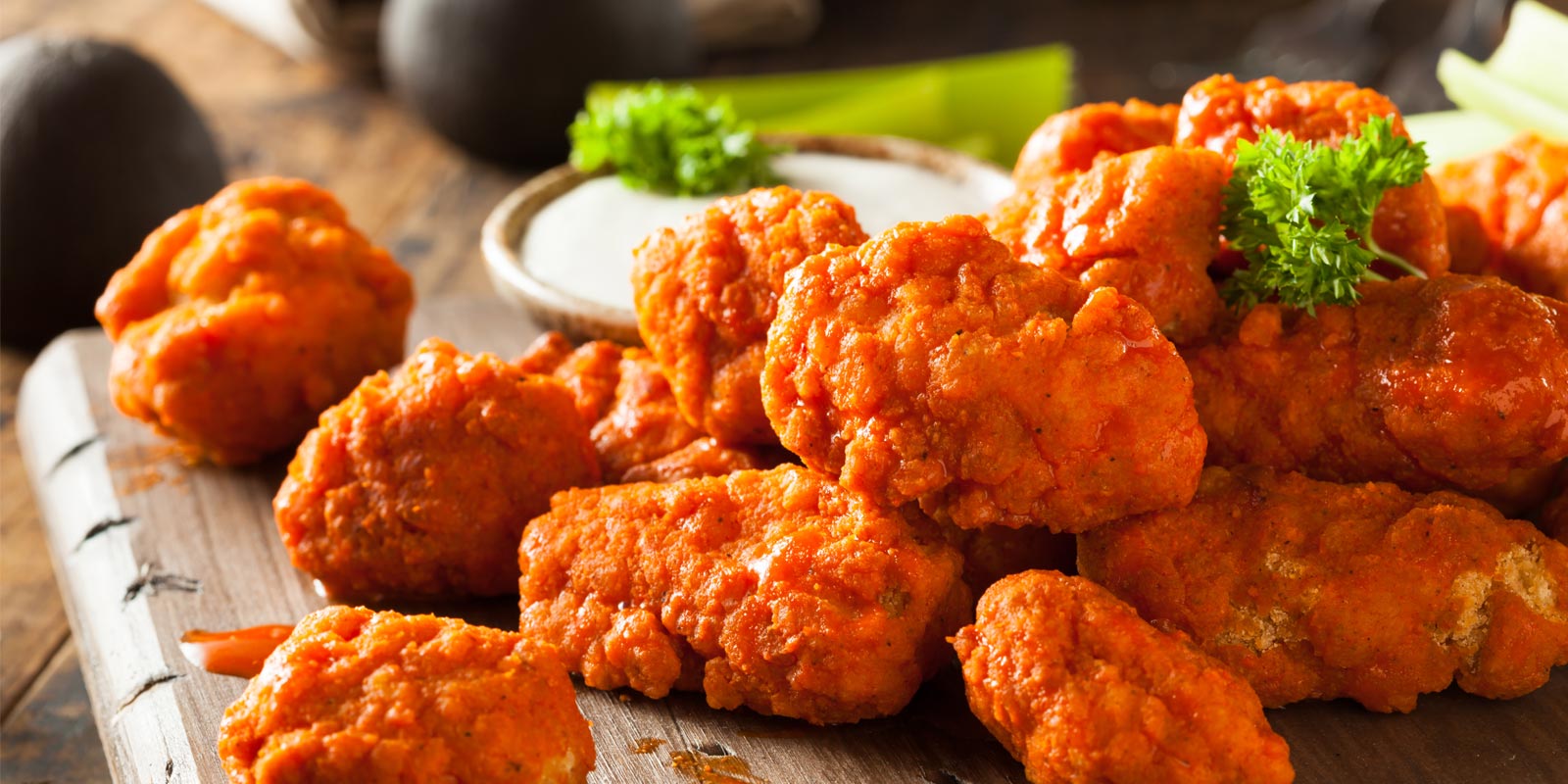 A spread of chicken bites with garnish and dip on a wooden serving dish.