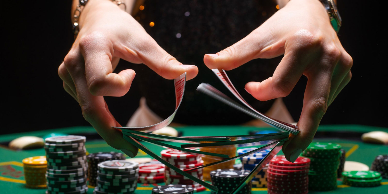 Hands shuffling cards over a poker table with poker chips.