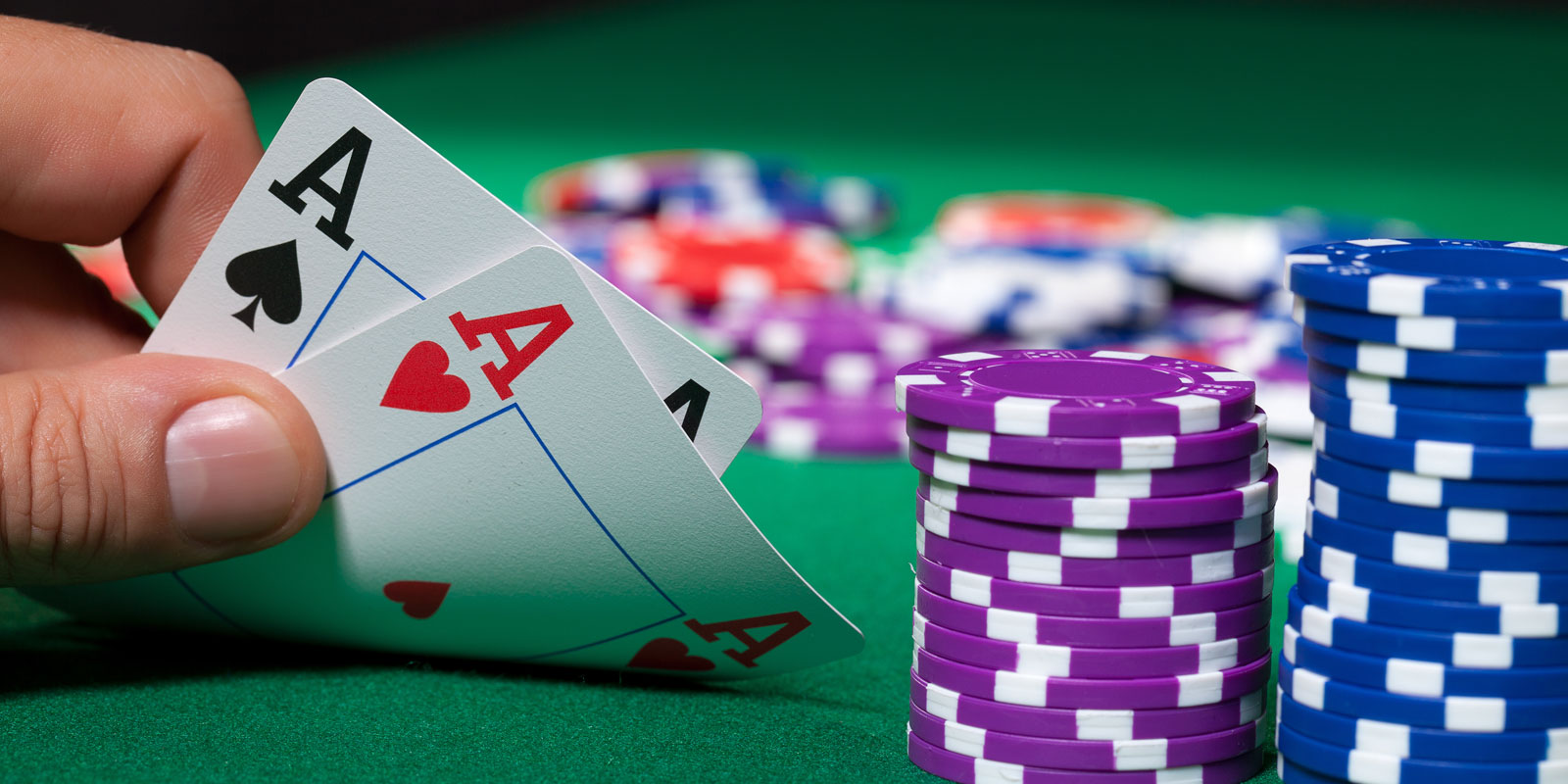 Hand holding a pair of aces with purple and blue poker chips