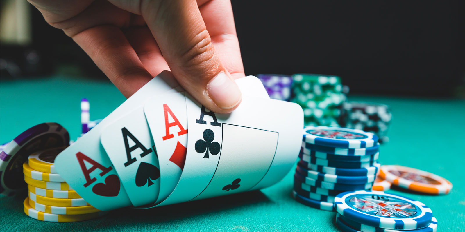 Hand holding four cards on a poker table with poker chips.
