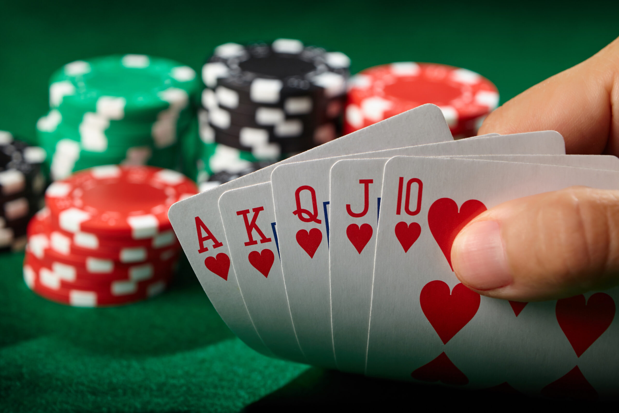 A hand holding a royal flush on a poker table with poker chips.